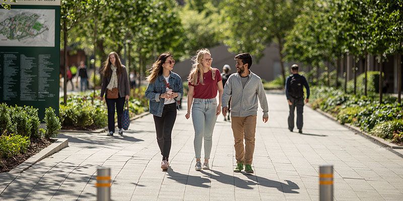 Three students exploring the University of Leeds campus on a sunny day — surrounded by trees.