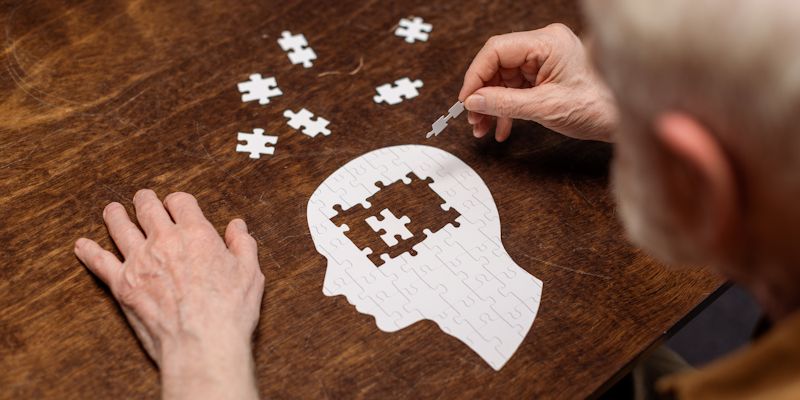 An elderly person doing a jigsaw puzzle shaped like a head. They are placing pieces in the area of the brain.