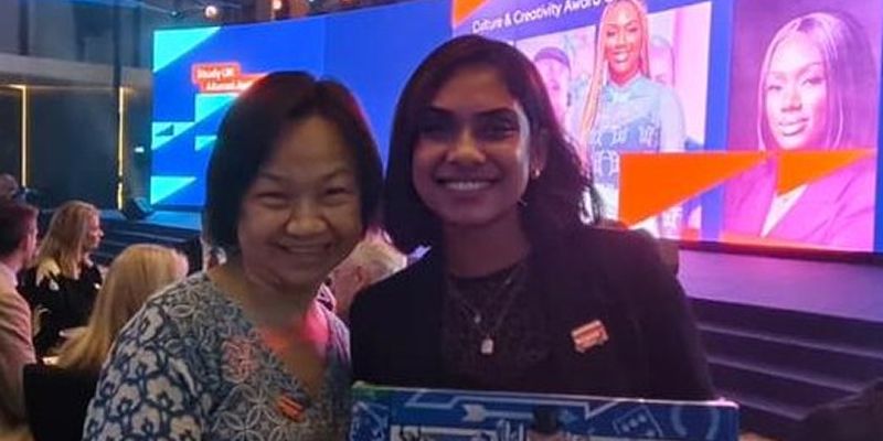 Senthilmani stands at an awards ceremony alongside a lady, smiling at the camera