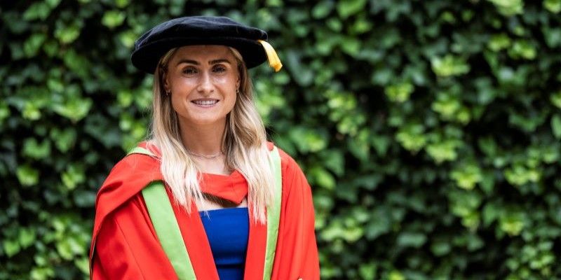 Steph Houghton stands in red and green graduation gowns.