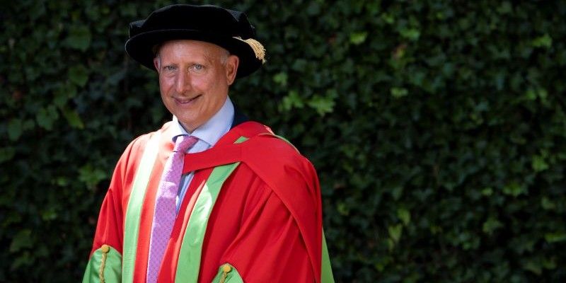 Steve Rosenberg wears honorary degree robes of red and green and smiles at the camera