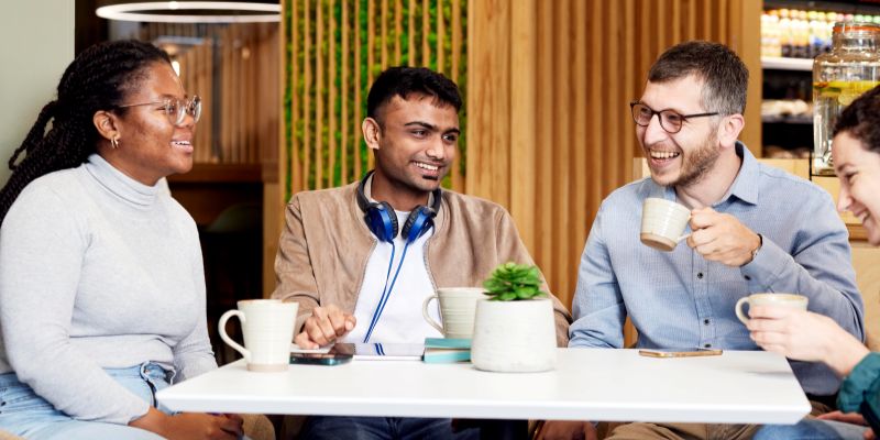 Front close view of four students sitting around a table, enjoying a coffee in a café on campus.