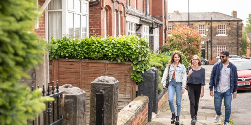 Three students walk along a street of terraced houses.