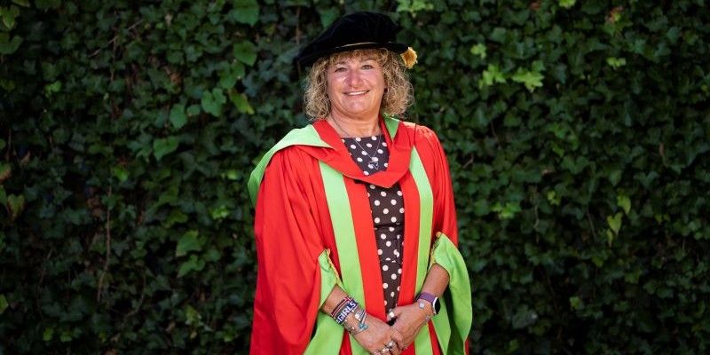 Tina Leslie MBE smiles at the camera as she wears her graduation robes