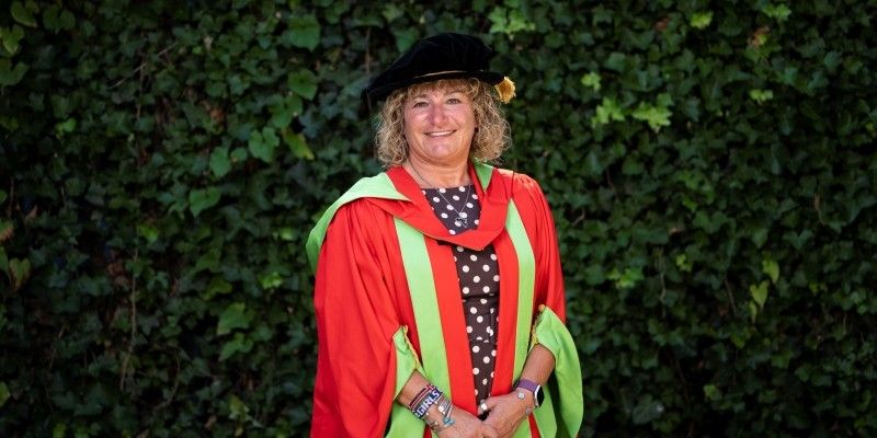 Tina Leslie stands smiling at the camera, in red and green graduation robes.