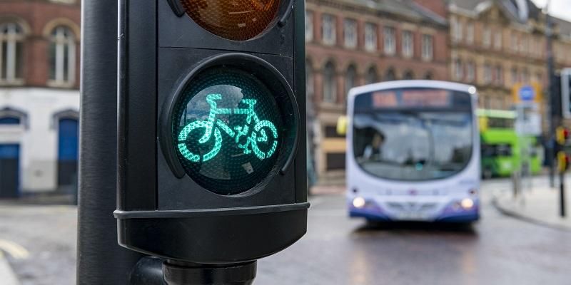 A traffic light on green for cyclists, with buses in the background