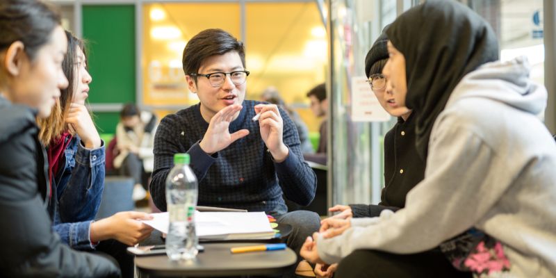 Close up of a group of five students sit at a small grey table.