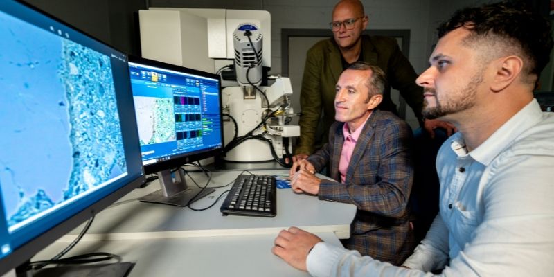 Three researchers look at brightly-coloured images on computer screens. They show the microstructure of concrete, from samples viewed under the nearby electron microscope.