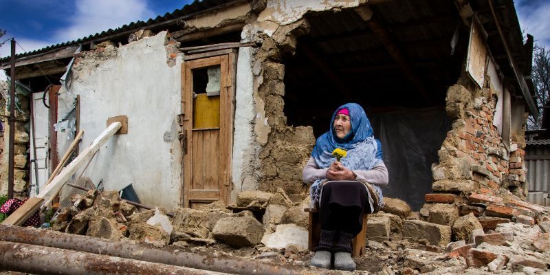 A woman prays in front of a destroyed house in the war in Ukraine