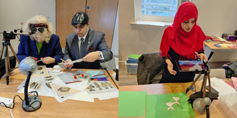 People taking part in a Welcoming Migrants collage workshop and stop-motion animation workshop. They are sat at a table cutting out shapes and using an iPad on a tripod to film some cut-out angel shapes.