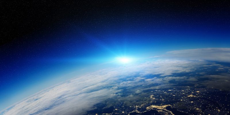 A view of the earth in space, with rays of light from the sun appearing on the horizon.