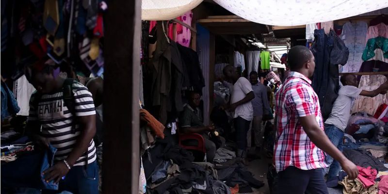 Kantamanto Market in Ghana. Several people are walking around the market amongst piles of clothes
