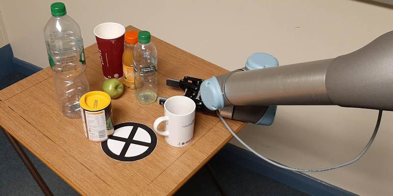 A robot arm attempts to navigate a number of objects on a table top, in order to get at an apple.
