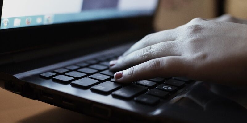 A hand typing on a keyboard with computer screen in the background