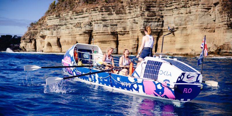 Team of three laugh on the rowing boat as they approach land at the end of the race