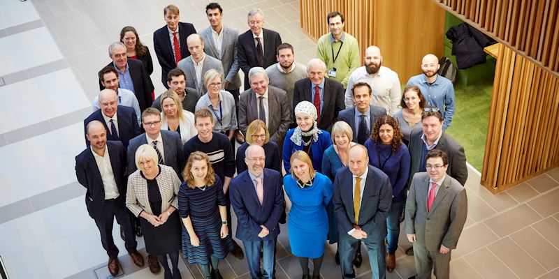 Cancer Research UK leaders and University of Leeds cancer scientists stand in a group of 25 looking up at camera