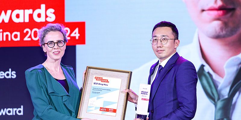 Woman in dress gives framed award to Bing Hou in suit