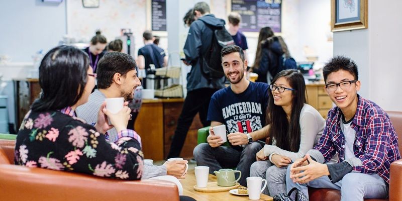 Five students are sat in a cafe on campus drinking coffee and chatting.