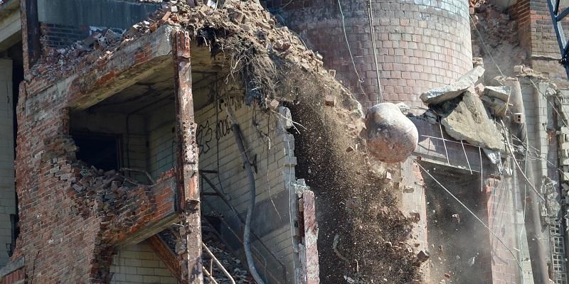 The image shows a wrecking ball being used to demolish an old factory