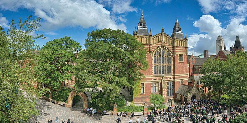 The Great Hall with trees and blue sky. Lots of people are gathered outside for graduation.