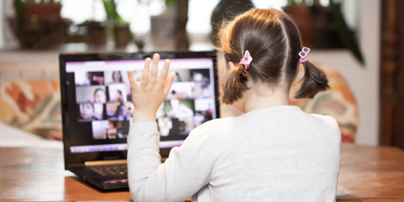 A young girl holding her hand up while on a video call with other children