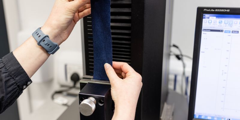 Hands holding denim as it is being tested in the Materials Testing Lab in front of a computer.