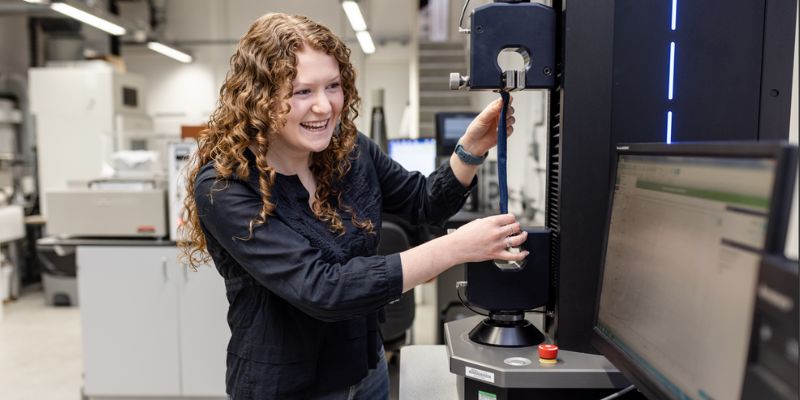 Phd student Kate Morris testing denim in a machine and looking at a computer in the Materials Testing Lab.