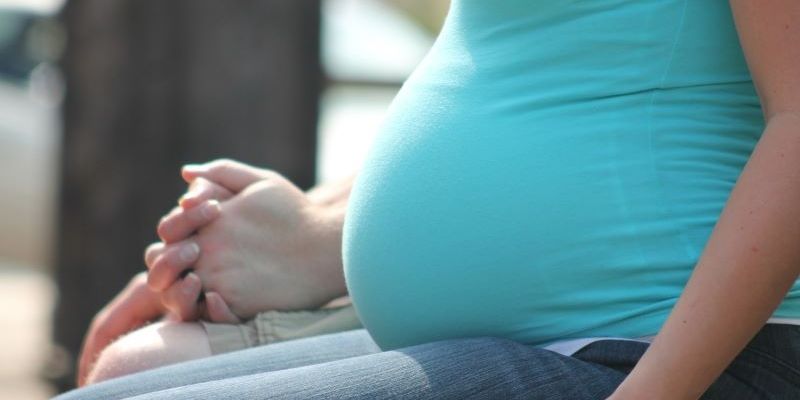 A pregnant woman sitting holding hands with a partner