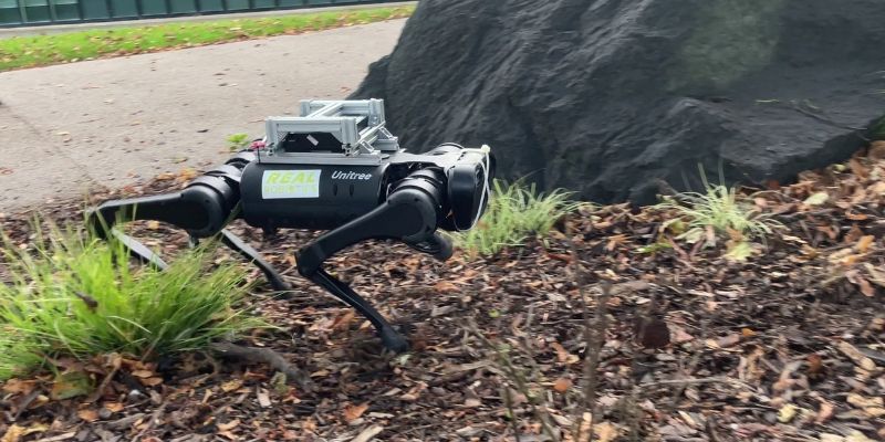 Four-legged dog-type robot walks on woodchip.