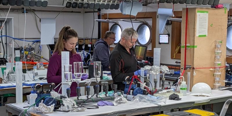 Researchers working with scientific equipment inside a laboratory on a research vessel.