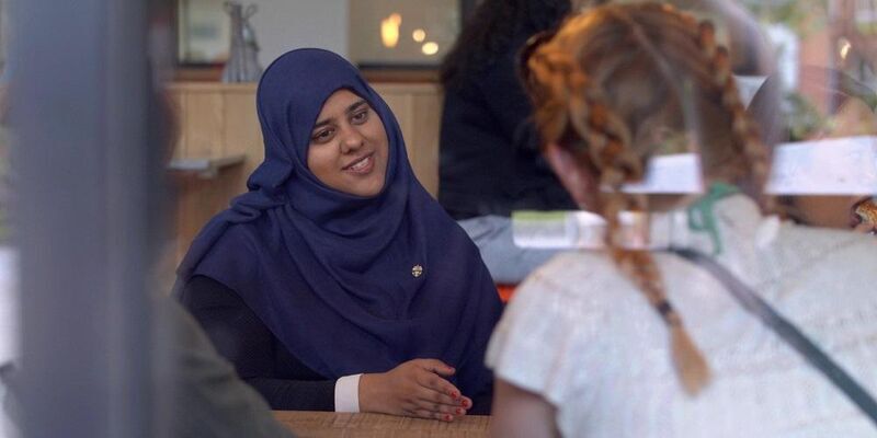 Two mature students chatting in a cafe. One is smiling.