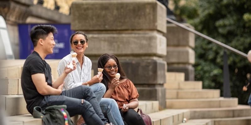 A small group of students sitting on the steps of Leeds Museum enjoying the sunshine and eating ice cream