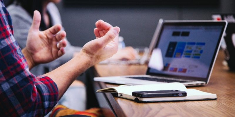Close up on two people's hands gesturing while looking at a laptop on a desk