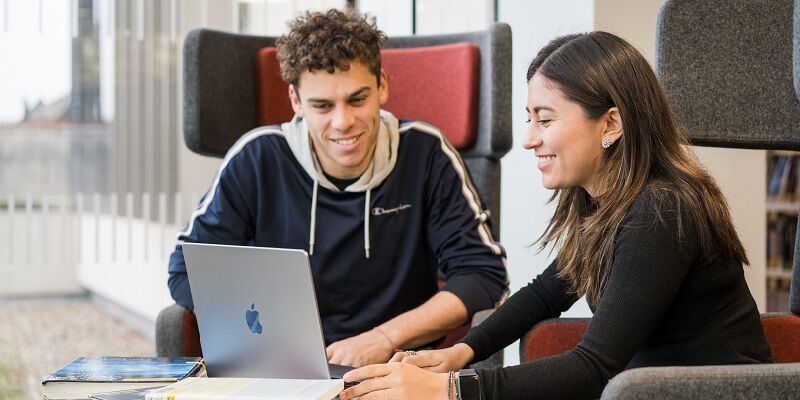 Two students sat in the Laidlaw library, using a laptop and smiling