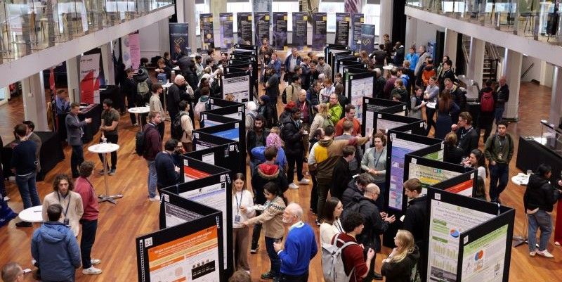 The Bragg Exchange event, with researchers gathered in a large, modern atrium discussing projects displayed on rows of presentation boards.