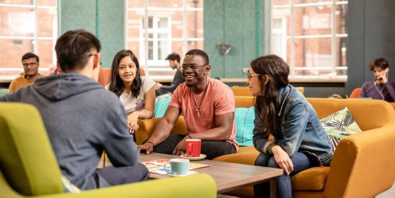 A group of students sit on sofas in a cafe area, smiling