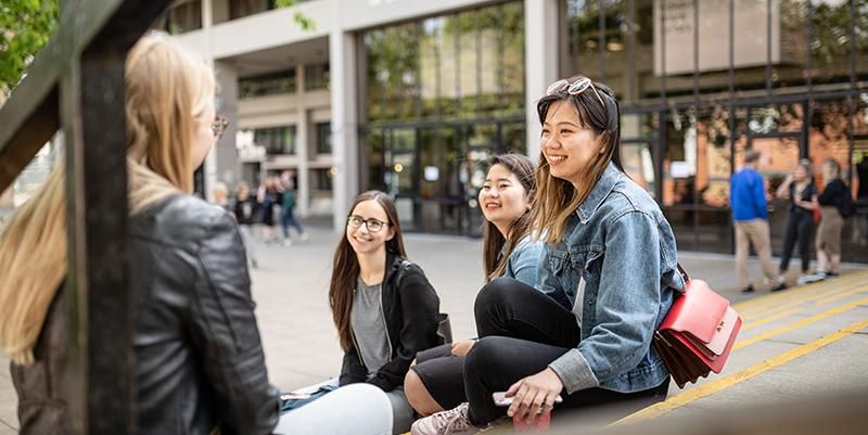 A group of students sit on some steps on campus smiling