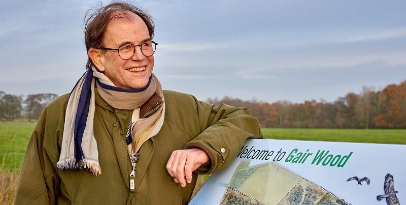 Roger Gair at Gair Wood, smiling and leaning on a sign.