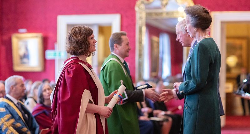 Amanda Maycock in foreground with red robe holding scroll and speaking to Princess Anne. Nick Plant in background in green robe speaking to Prince Charles. 
