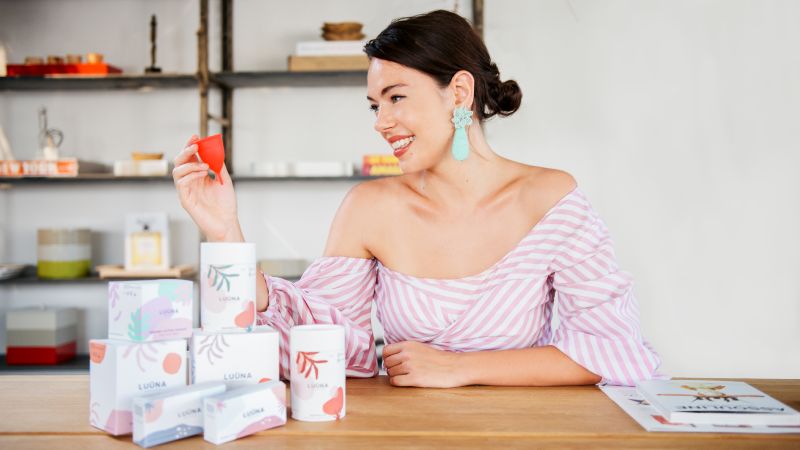 Olivia Cotes-James sat at a table with boxes of LU&Uuml;NA Naturals products on the table.