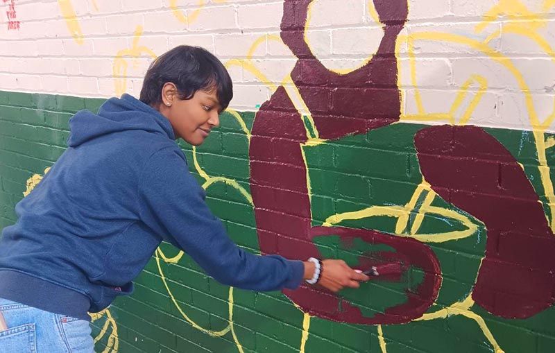 Tanvi starting work on painting the mural on a brick wall.