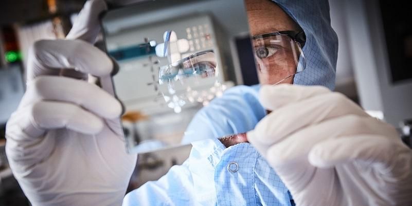 Scientist in protective clothing holding and examining a slide.