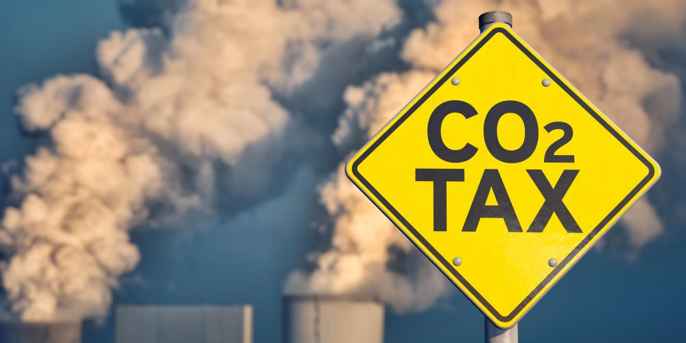A sign saying CO2 tax in front of a power plant releasing vapour into the atmosphere.