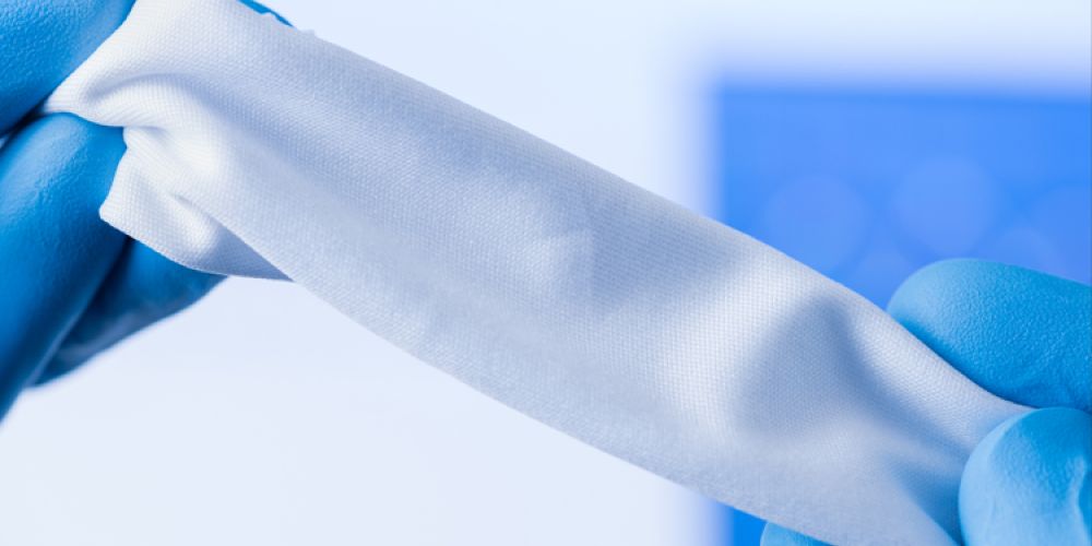 White cloth held in hands wearing blue nitrile gloves.