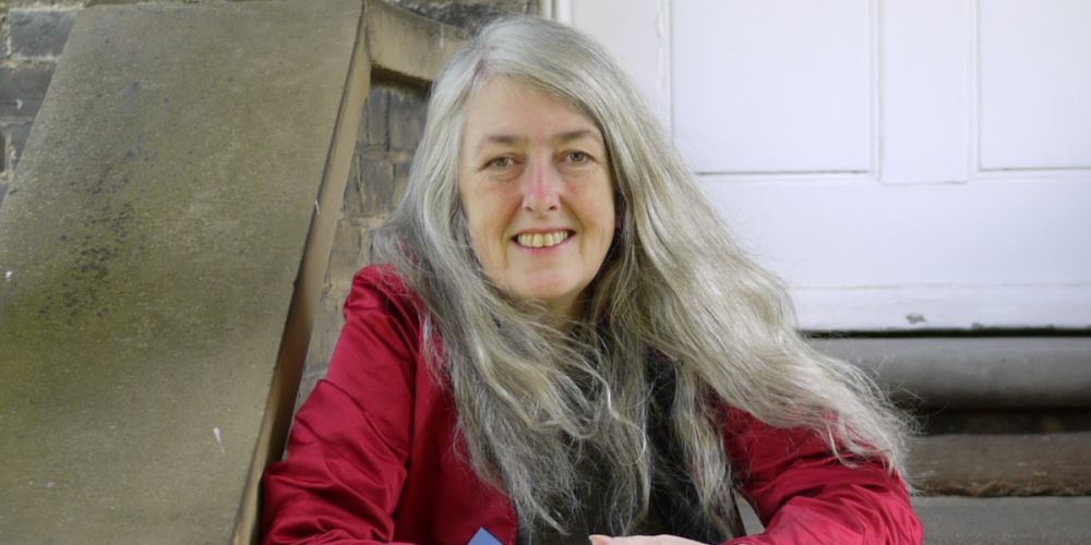 Professor Mary Beard sitting on an outdoor staircase and smiling at the camera