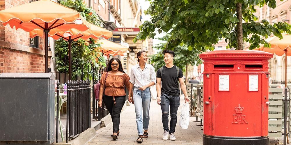 Three students walking next to a red post box in Leeds city centre
