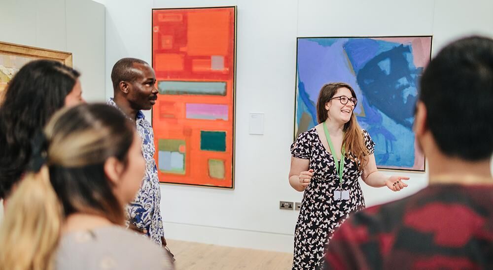 A galleries staff member talking to a group in front of a painting in the Stanley and Audrey Burton Gallery.