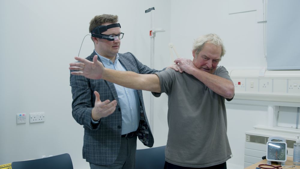 A doctor examines a patient&#039;s shoulder in a consulting room, using virtual clinical experiences glasses, which enables the examination to be live-streamed