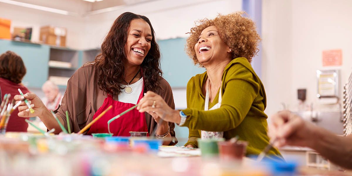Two women laughing whilst painting in an art studio.