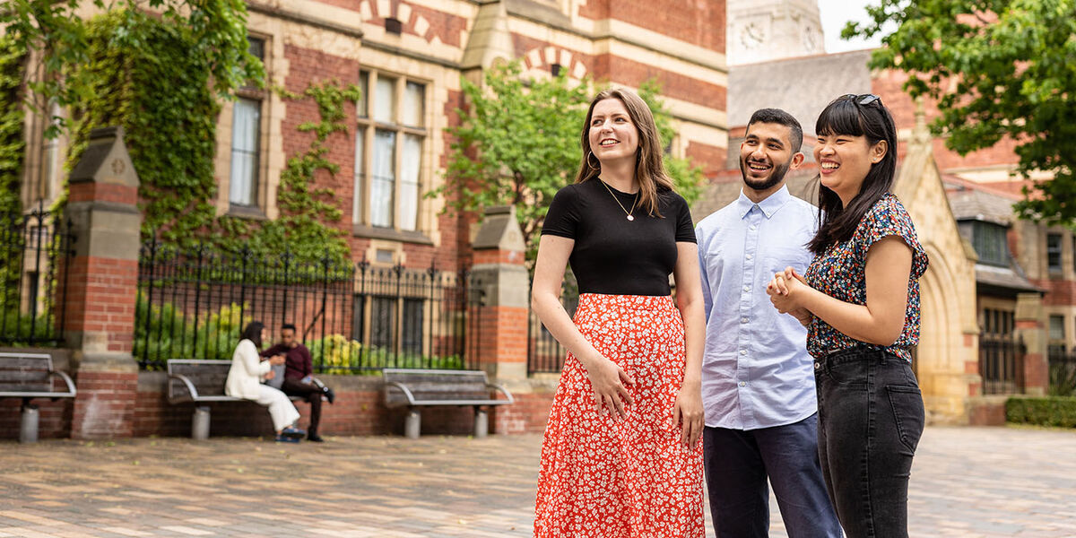 Three postgraduate students on campus outside The Great Hall.